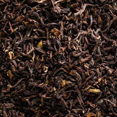 Kupferbraune Darjeeling-Teeblätter mit Tips neben einer rötlich-bernsteinfarbenen Tasse Second Flush Tee